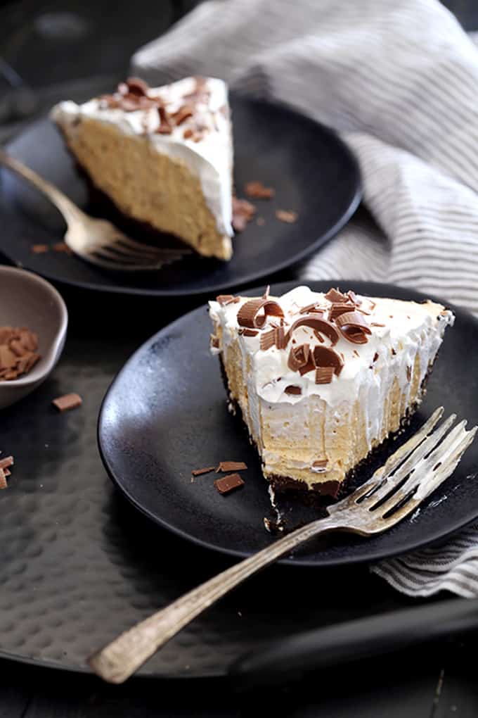 A slice of Black Bottom No Bake Pumpkin Cheesecake with a bite removed and on a fork, sits on a black plate with a striped napkin in the background.