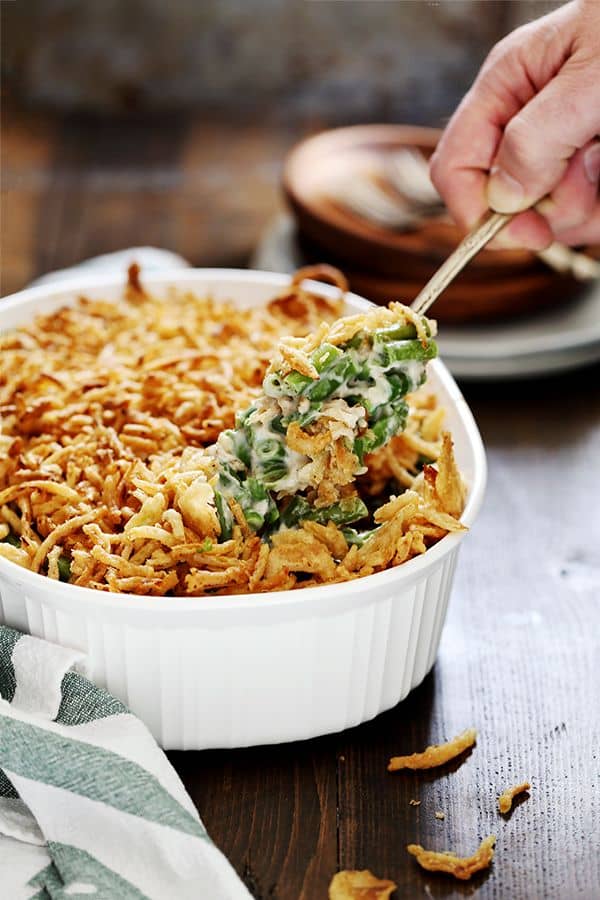 A scoop of Twice the Onion Green Bean Casserole is being lifted out of a white casserole dish.