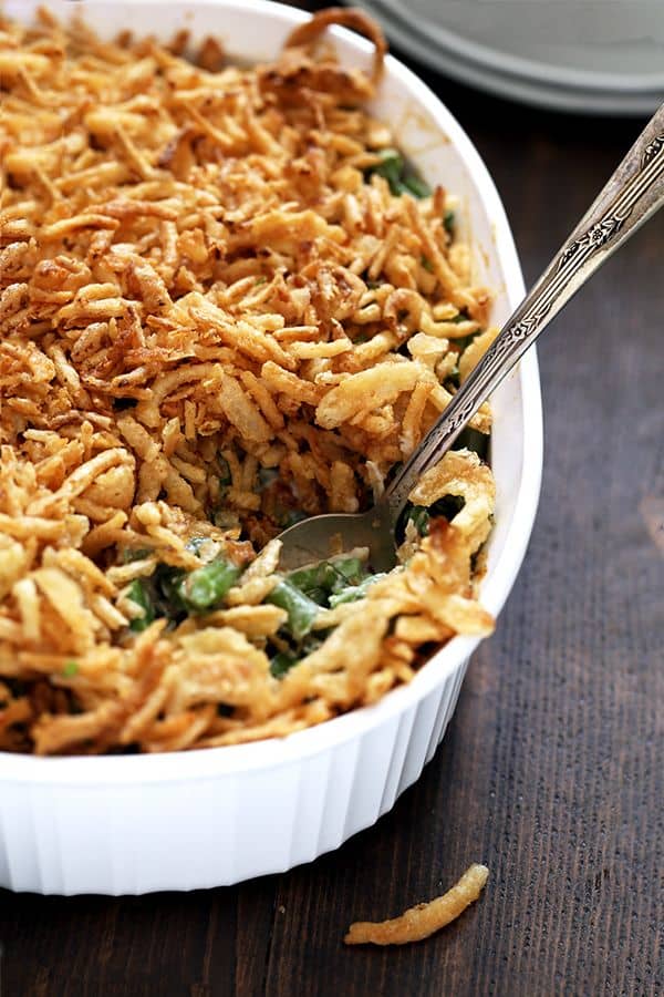 A scoop of Twice the Onion Green Bean Casserole is being lifted out of a white casserole dish.
