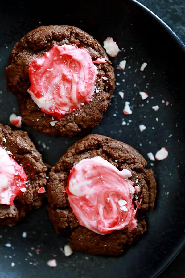 Three Mocha Peppermint Crunch Cookies sit on a black plate showered with crushed peppermint.