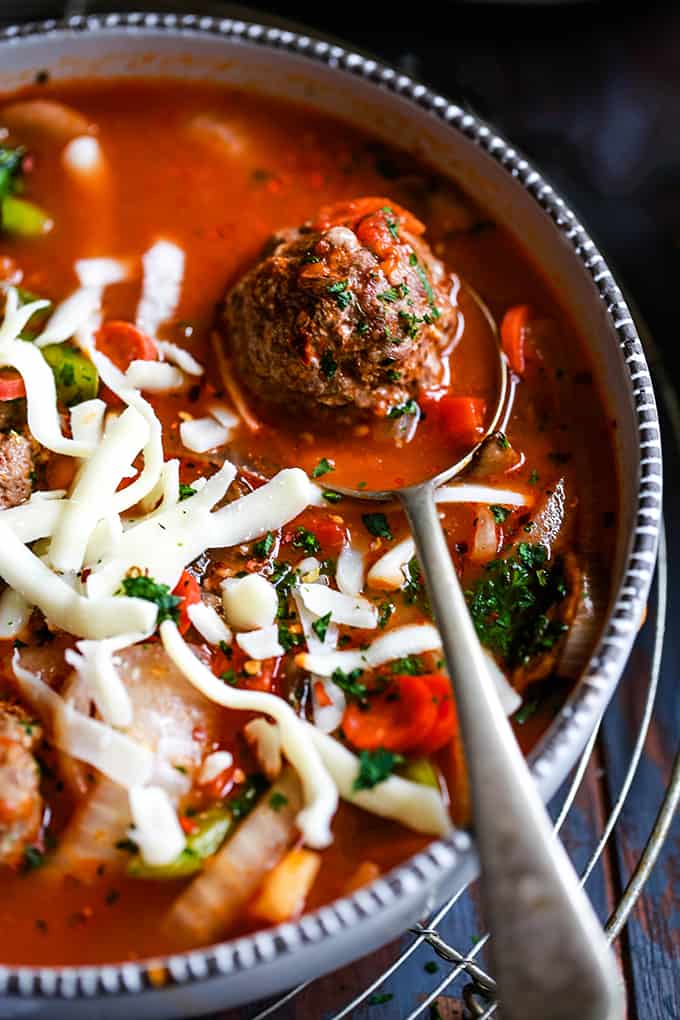 A meatball rests on a spoon in the middle of a bowl of Meatball Pizza Soup.
