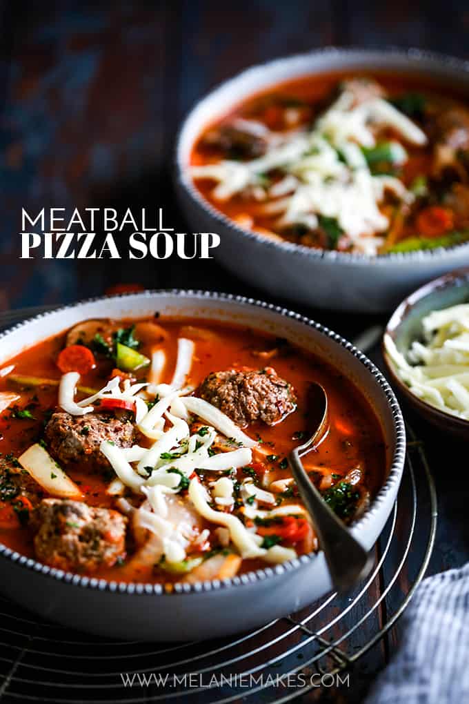 Two bowls of Meatball Pizza Soup, one with a spoon and sitting on a wire rack.