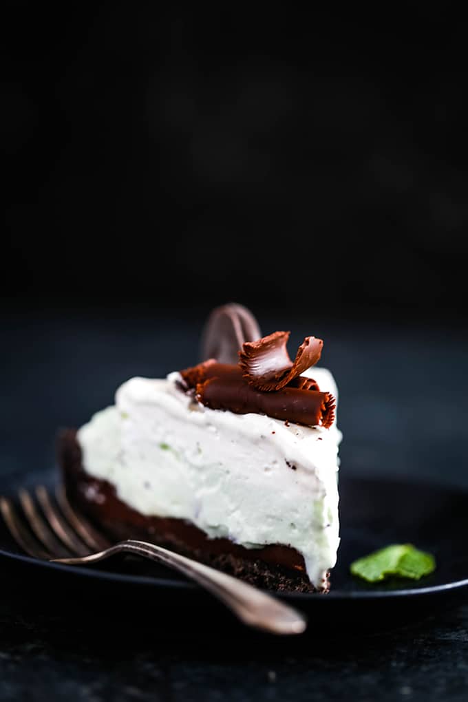 A slice of Grasshopper Ice Cream Tart sits on a black plate with a fork and a garnish of fresh mint.