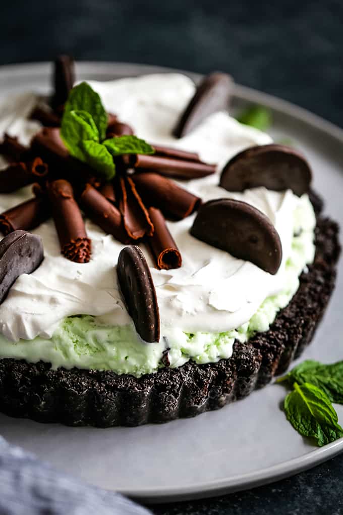A Grasshopper Ice Cream Tart is garnished with mint cookies, chocolate curls and fresh mint.