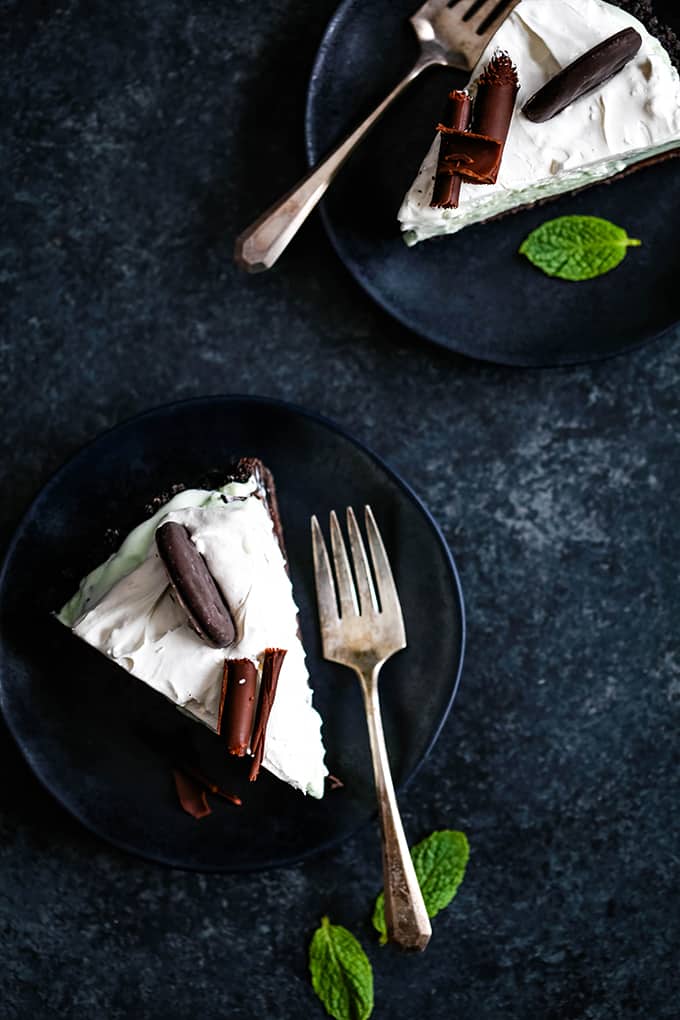 Two slices of Grasshopper Ice Cream tart sit on plates with forks and garnished with fresh mint leaves.