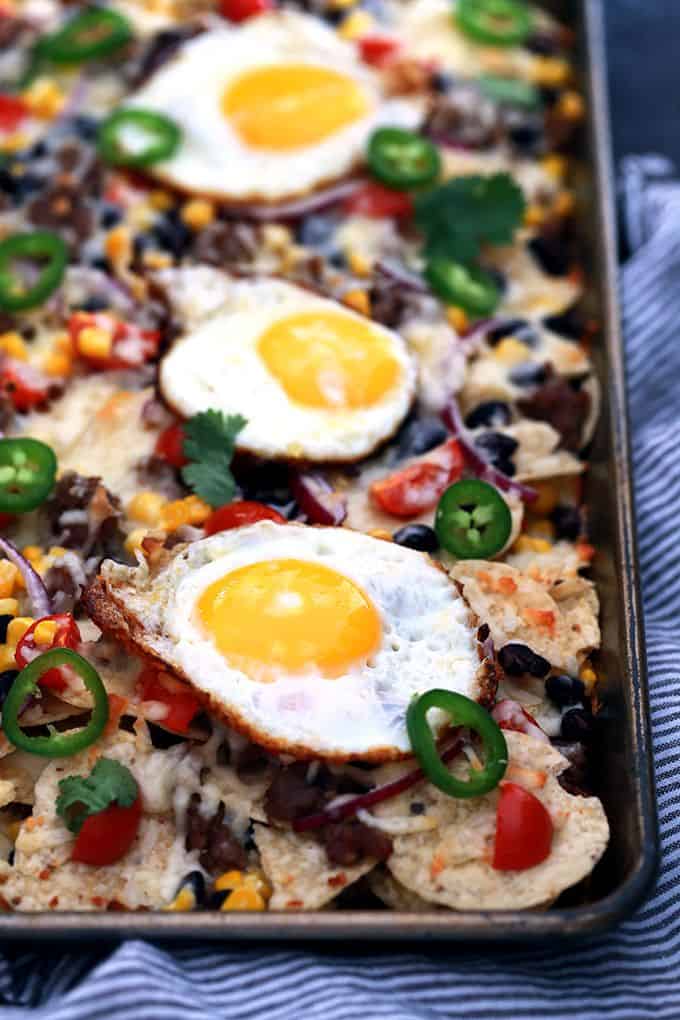 Huevos Rancheros Sheet Pan Nachos are a quick and delicious recipe perfect for feeding an entire family easily. Layers of chips, black beans, cherry tomatoes, corn and melty Monterey Jack cheese are topped with sunny side up eggs. Great for breakfast but also for an appetizer or brinner, too!