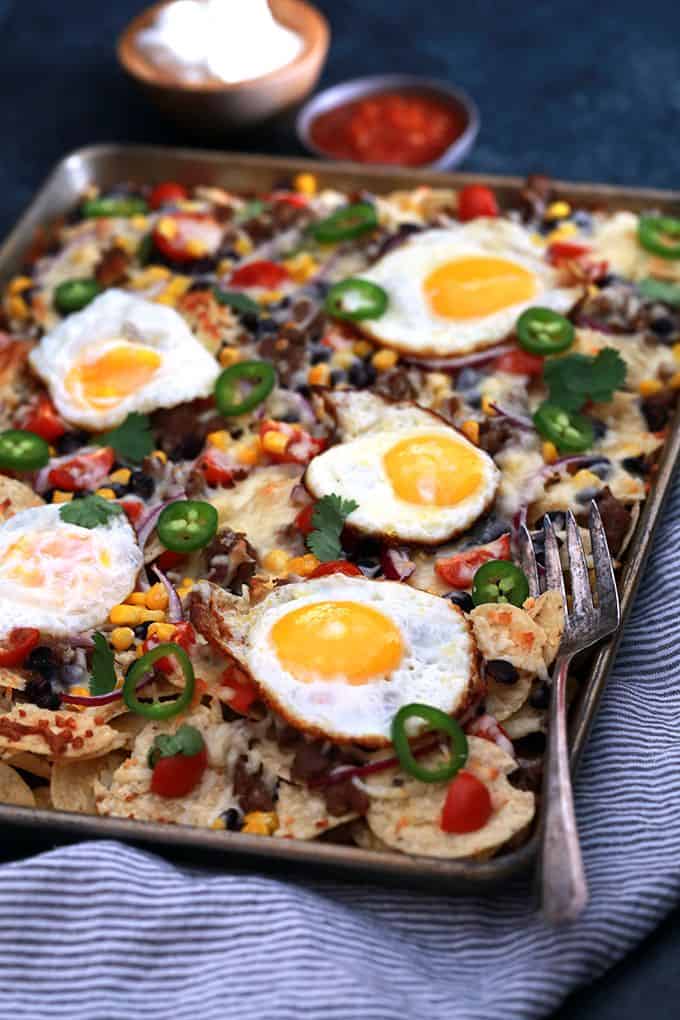 Huevos Rancheros Sheet Pan Nachos are a quick and delicious recipe perfect for feeding an entire family easily. Layers of chips, black beans, cherry tomatoes, corn and melty Monterey Jack cheese are topped with sunny side up eggs. Great for breakfast but also for an appetizer or brinner, too!
