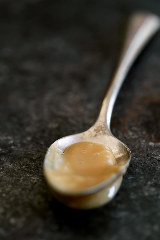 A spoon of dulce de leche rests on a black surface.