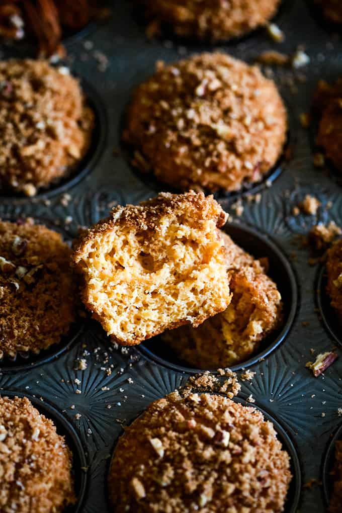 A split Butterscotch Muffin with Brown Sugar Pecan Streusel sits in a muffin tin.
