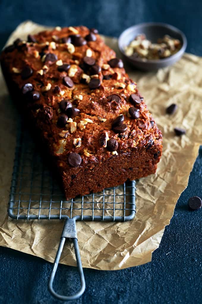 A loaf of Chocolate Chip Walnut Pumpkin Bread rests on a wire rack on a piece of parchment paper.