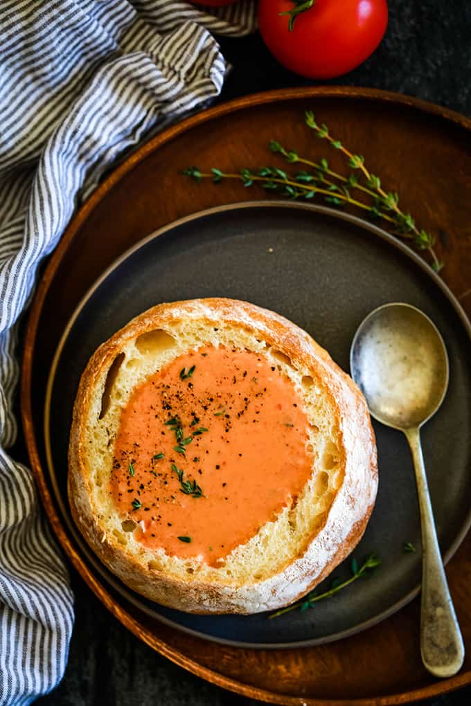 An overhead view of a bread bowl filled with Creamy Tomato Bacon Soup garnished with fresh thyme.
