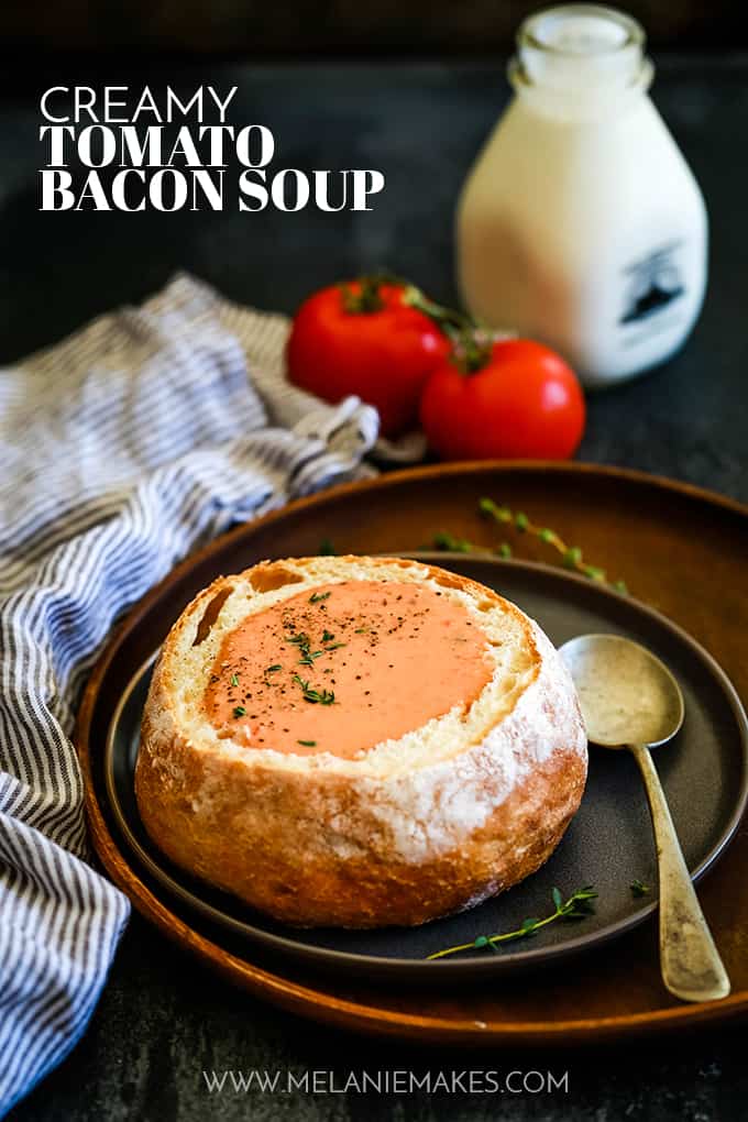 Creamy Tomato Bacon Soup in a bread bowl on a dark plate and wood platter.