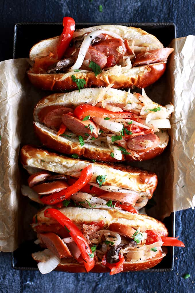 Four Slow Cooker Sausage and Sauerkraut Sandwiches on brown parchment paper in a metal pan on a black background.