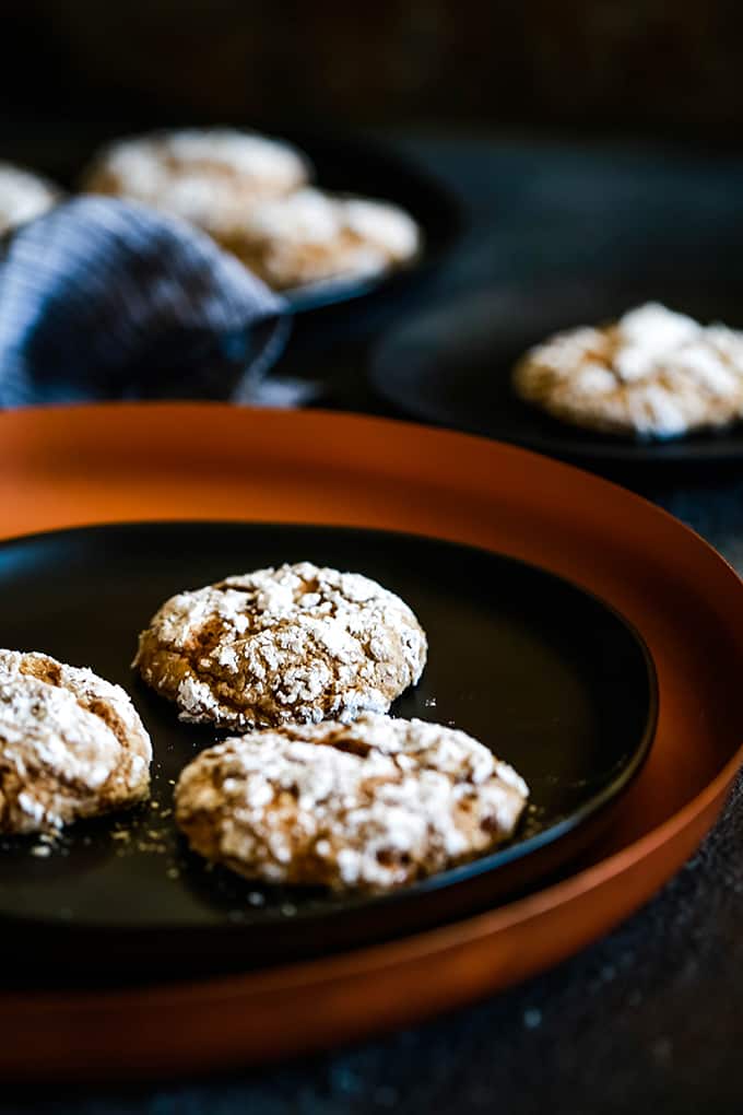 Caramel Pumpkin Spice Crinkle Cookies on a black plate sitting on a copper colored charger with two additional plates in the background.