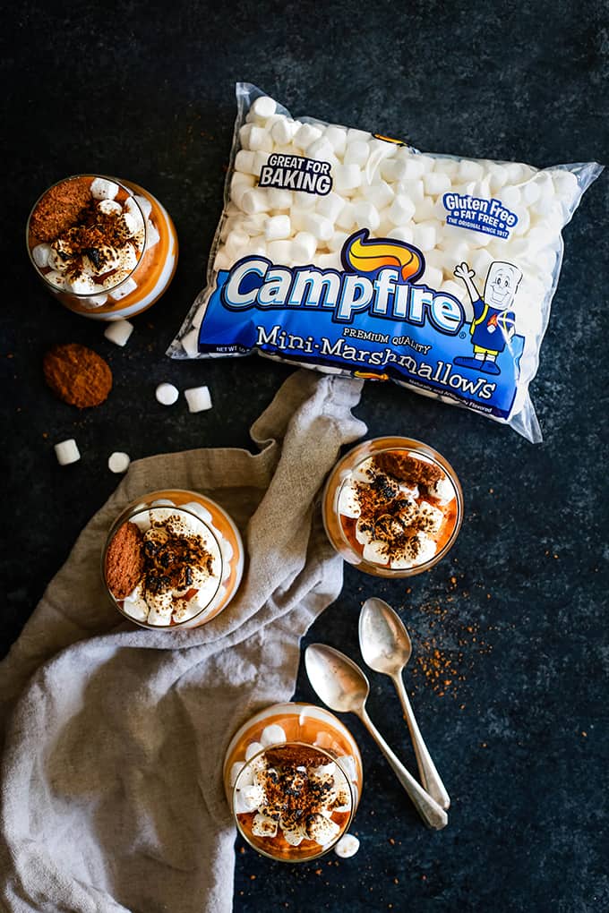 An overhead shot of four Gingersnap Sweet Potato Mousse desserts surrounded by a two spoons, a bag of Campfire Mini Marshmallows and a neutral colored napkin.