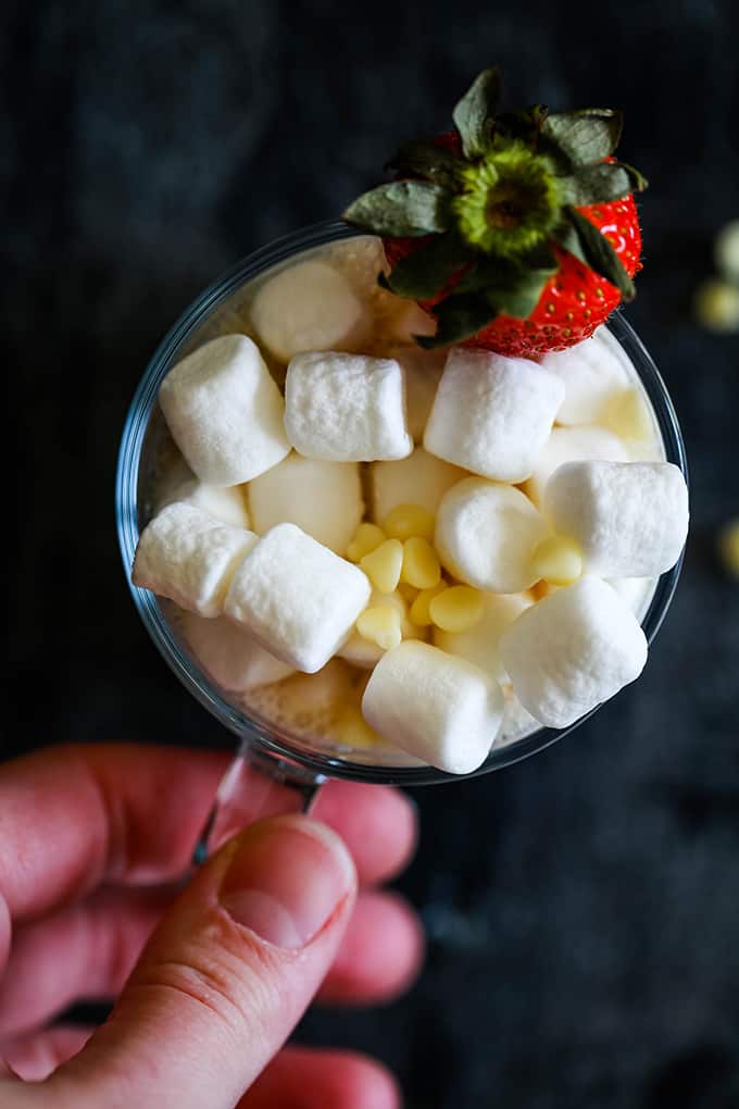 An overhead shot of a mug of Slow Cooker Strawberry Hot Chocolate topped with marshmallows, white chocolate chips and a strawberry on a white background.