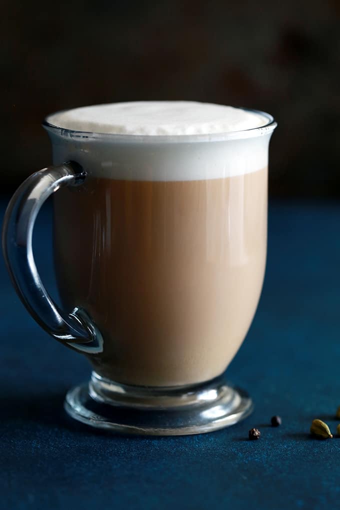 A chai latte in a glass mug made from Homemade Chai Tea Concentrate sits on a blue background.