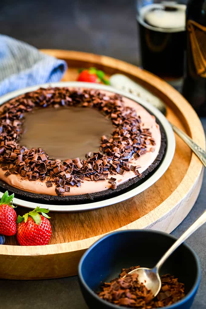 A No Bake Guinness Chocolate Cheesecake on a wooden tray with a pie server and strawberries.