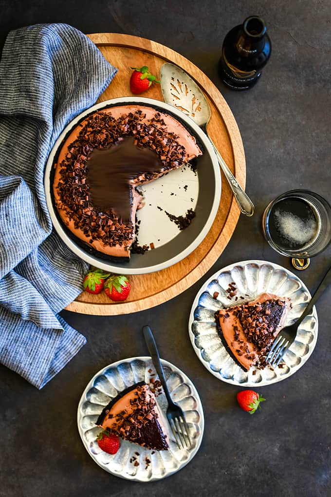 An overhead view of a No Bake Guinness Chocolate Cheesecake sitting on a wooden tray with two slices removed and sitting on silver plates.