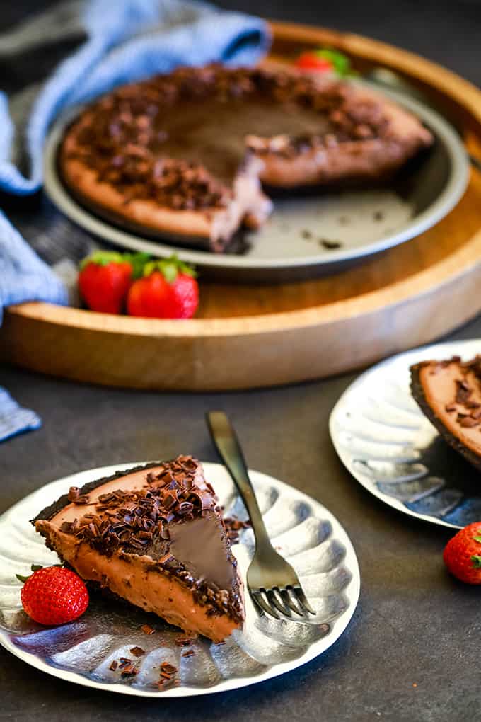A slice of No Bake Guinness Chocolate Cheesecake sits on a silver plate with a black fork and strawberry.