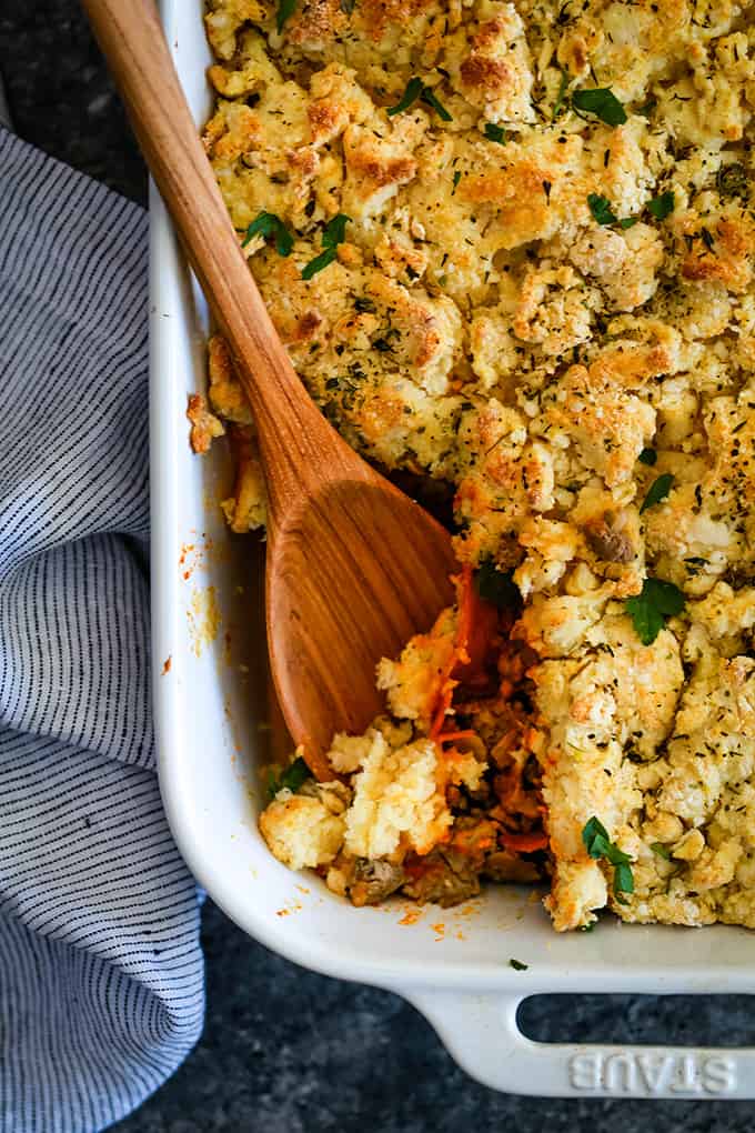 A wooden spoon in a white baking dish of Upside Down Pizza Casserole.