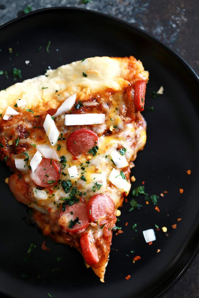 This Chili Cheese Dog Pizza begins with a homemade pizza dough layered with hearty chili and  shredded Mexican cheese before being topped with sliced hot dogs.  It's then garnished with chopped onion and cilantro before being cut into wedges and served.  Easy enough for any weekday, yet the perfect way to kick off a weekend. 