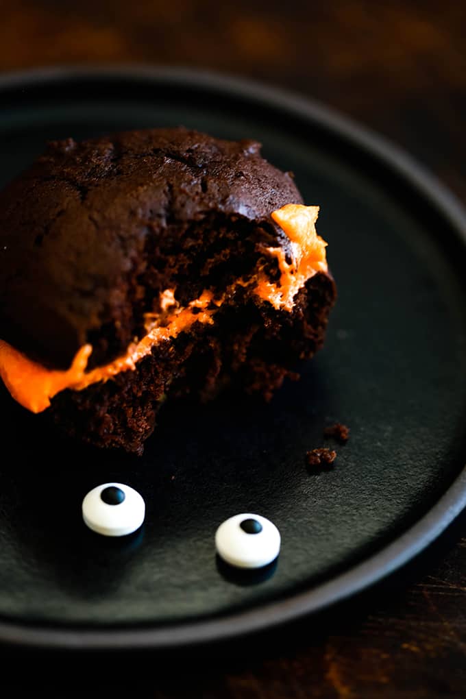 A Mini Monster Chocolate Whoopie Pie with a bite removed sits on a black plate with two candy eyes sitting on the plate.