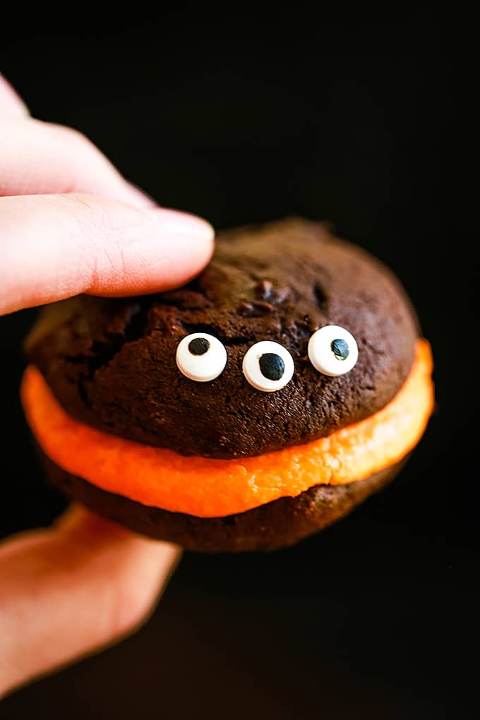 A hand holds a Mini Monster Chocolate Whoopie pie with three candy eyes.