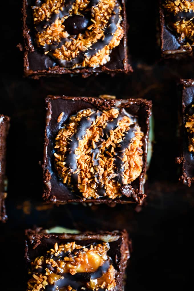 This decadent Samoa Brownies recipe has it all! Fudgy brownie, two layers of Samoa Girl Scout cookies, dulce de leche, coconut and chocolate ganache. #brownies #chocolate #cookies #caramel #coconut #desserts Samoa Brownies sitting on a dark surface.