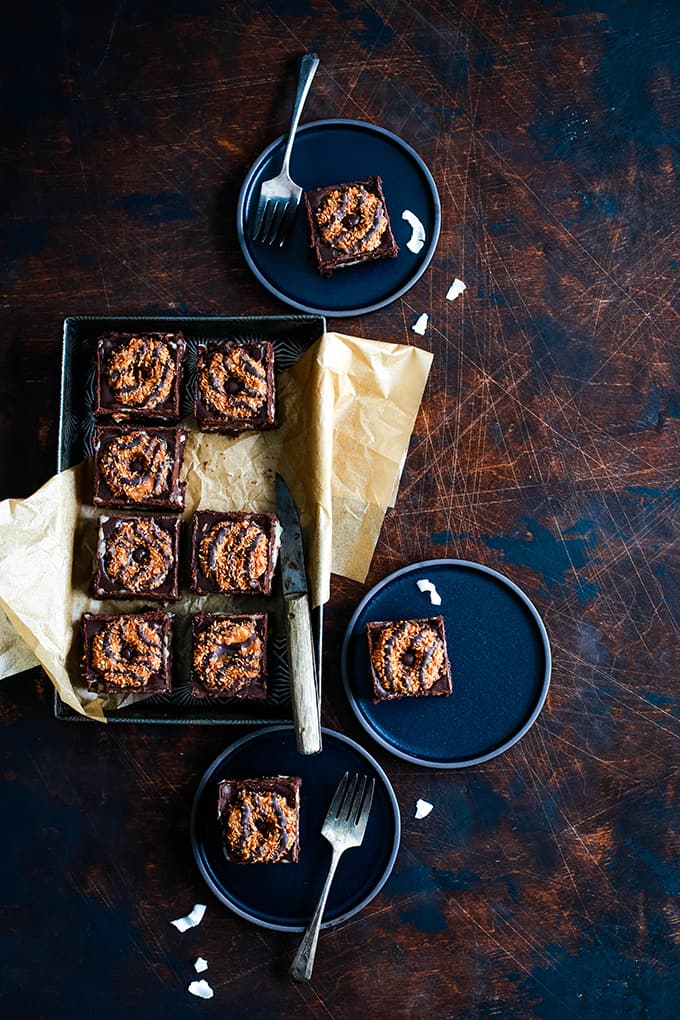 This decadent Samoa Brownies recipe has it all! Fudgy brownie, two layers of Samoa Girl Scout cookies, dulce de leche, coconut and chocolate ganache. #brownies #chocolate #cookies #caramel #coconut #desserts An overhead view of a pan of Samoa Brownies surrounded by three black plates with brownies.
