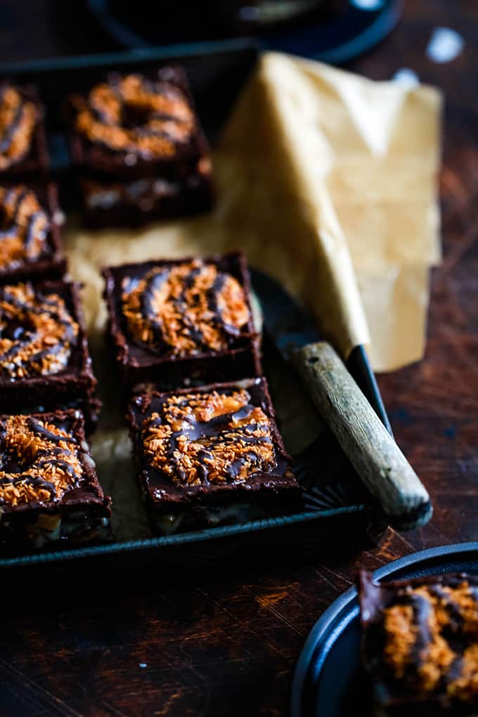 This decadent Samoa Brownies recipe has it all! Fudgy brownie, two layers of Samoa Girl Scout cookies, dulce de leche, coconut and chocolate ganache. #brownies #chocolate #cookies #caramel #coconut #desserts A pan of Samoa Brownies with a wooden handled knife.